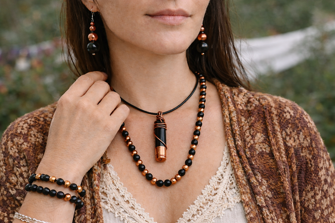 Bohemian layered jewelry worn on a model outdoors — shungite and copper beaded necklace with a slightly longer shungite pendant on black cord, matching bracelet and dangling earrings, styled in natural earthy clothing.