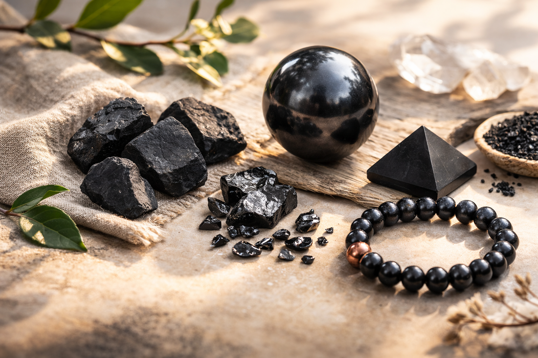 Flat lay of different types of shungite including raw black stones, small elite shungite fragments, a polished sphere, pyramid, and shungite bead bracelet arranged on natural linen in warm sunlight