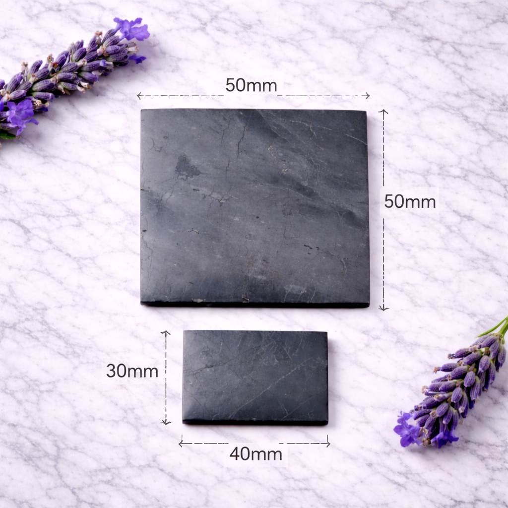 Two polished shungite plates in different square sizes displayed on a white marble surface, accented with purple lavender sprigs, showing natural stone veining and matte black texture.
