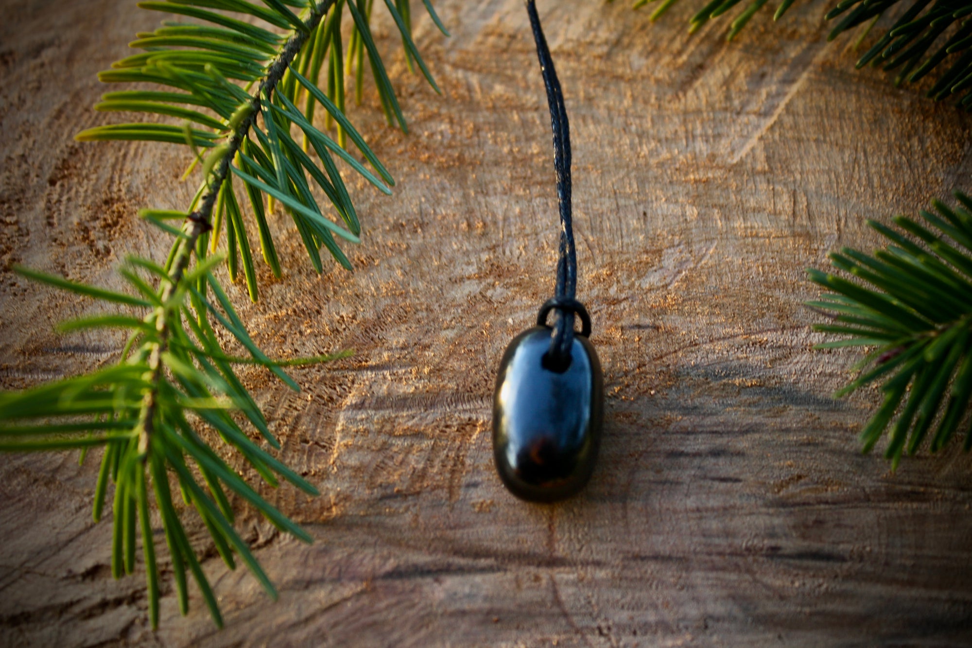 Tumble Shungite stone pendant with a smooth, polished finish, featuring a hole and adjustable string for a stylish and protective necklace.