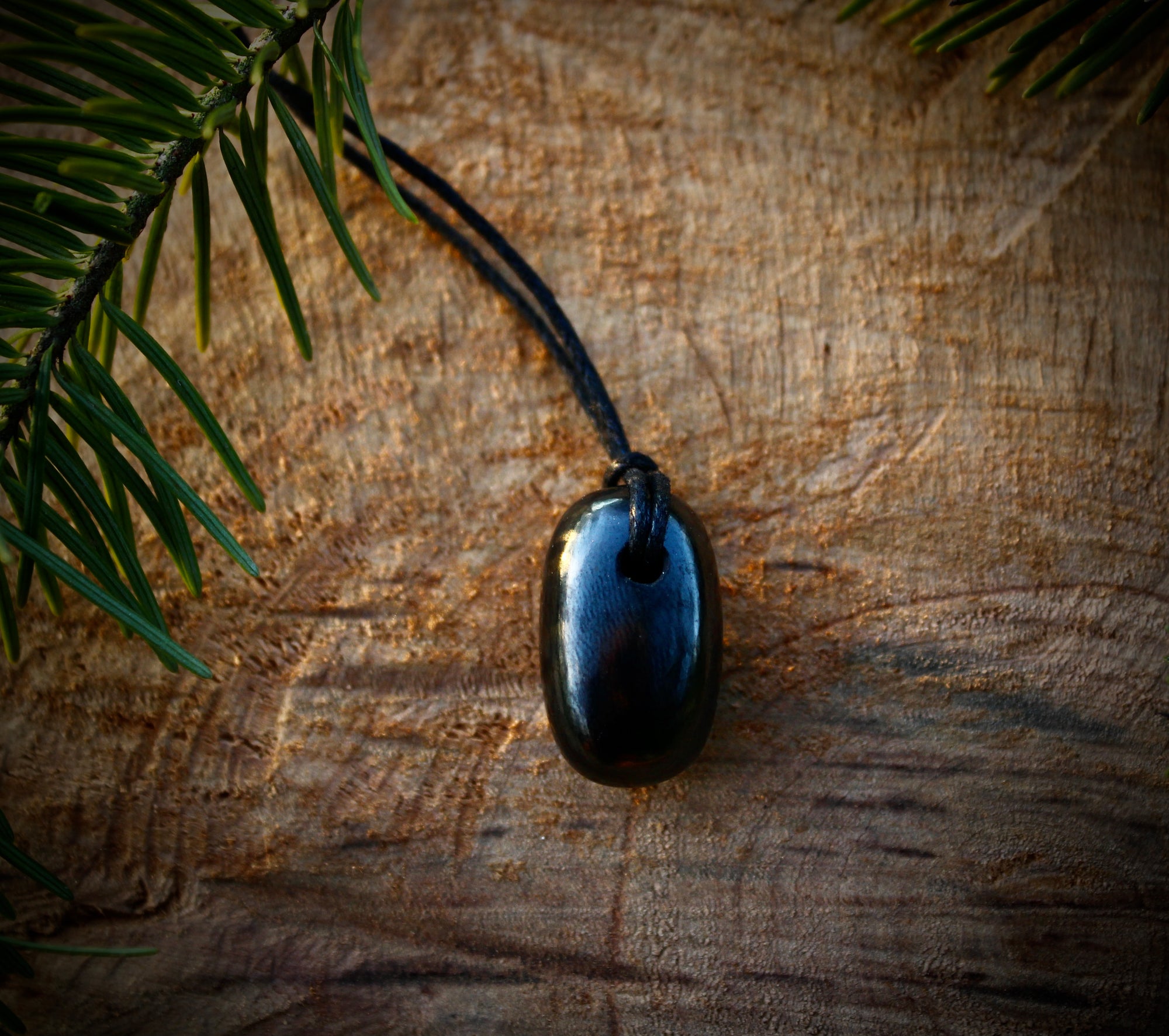 Tumble Shungite stone pendant with a smooth, polished finish, featuring a hole and adjustable string for a stylish and protective necklace.