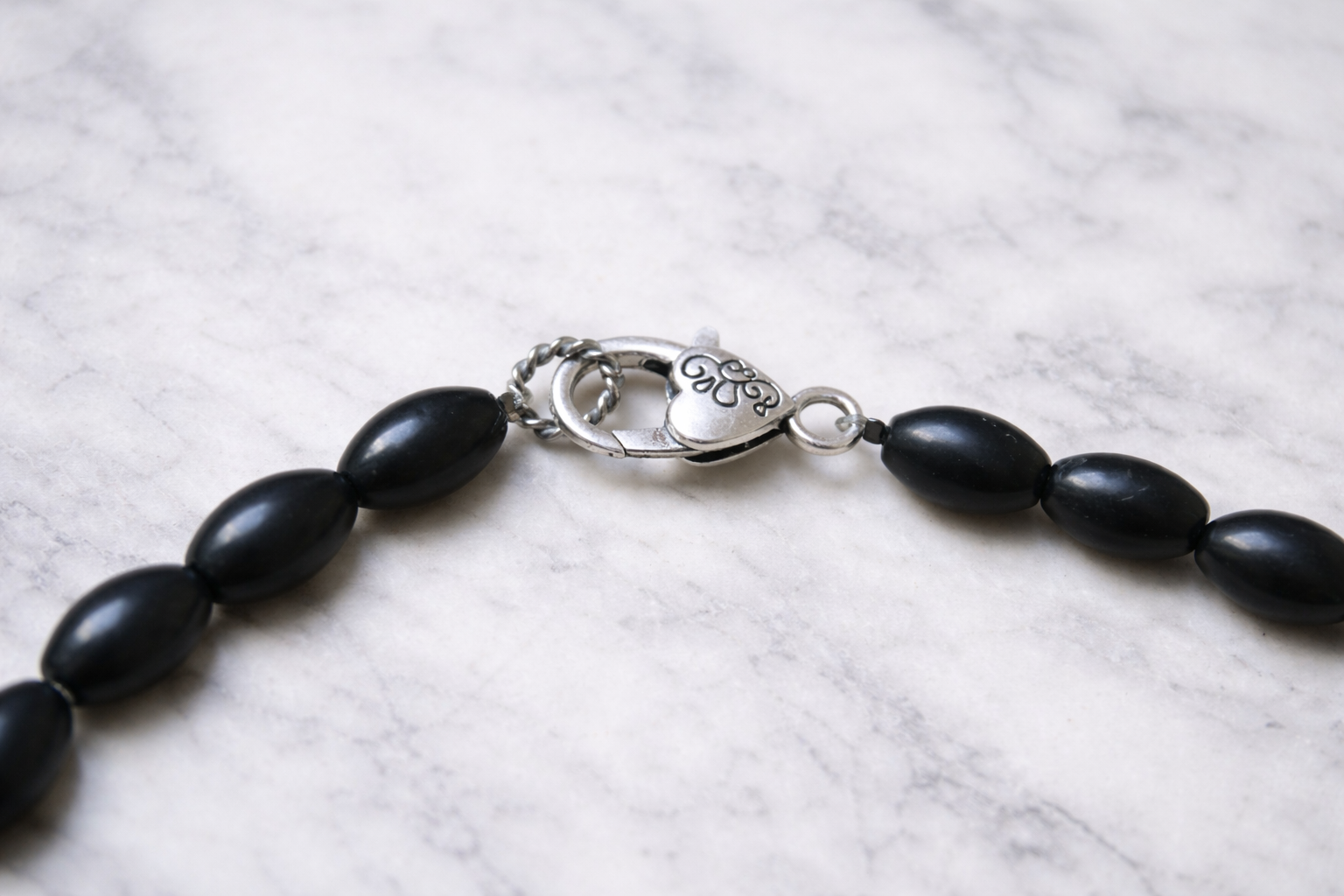 Close-up of silver lobster clasp and black shungite beads from handmade necklace resting on a light marble surface with soft natural lighting