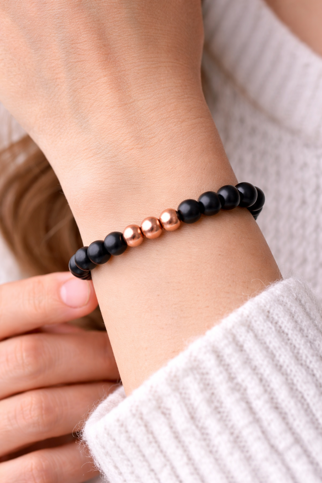 Black shungite beaded bracelet with three polished copper center beads resting on a white marble stone, photographed from a side angle with soft natural lighting.