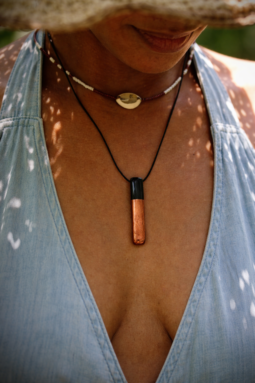 “Copper and shungite pendant hanging on black cord worn outdoors in soft natural light”
