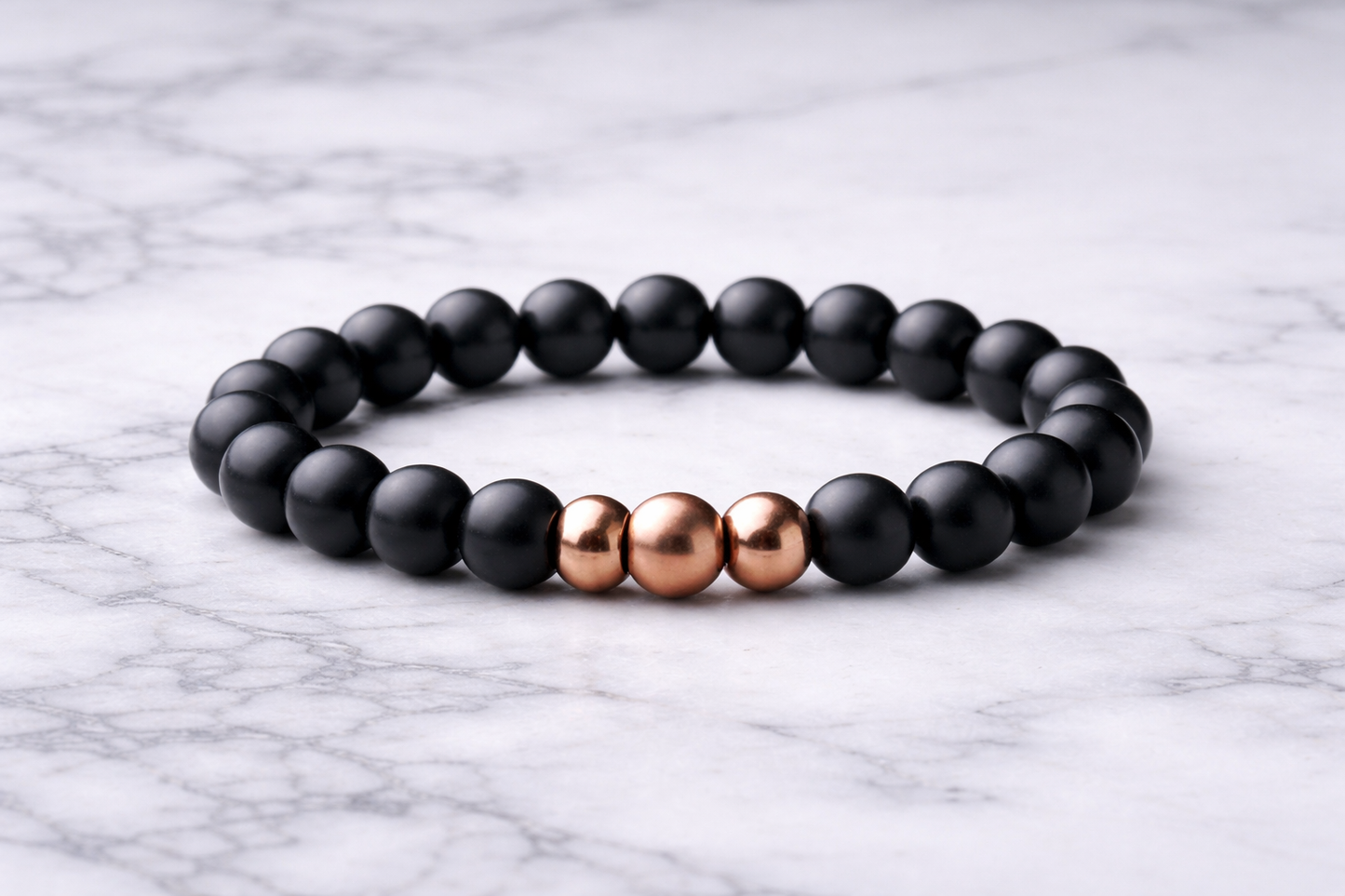 Matte black shungite bead bracelet with three copper accent beads centered, displayed on a white marble background.