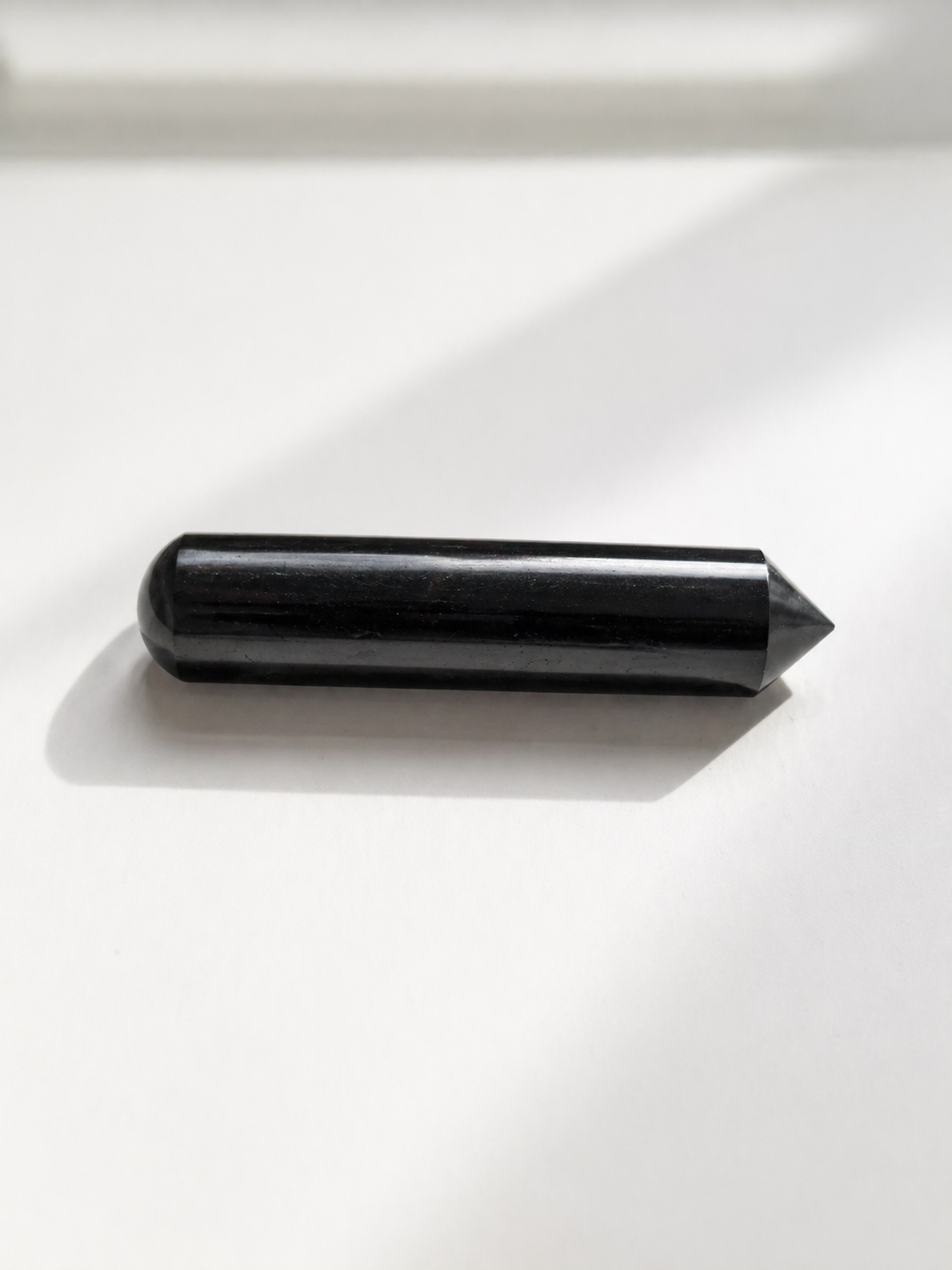 Polished shungite massage stick with pointed tip on white background with soft natural light and shadow