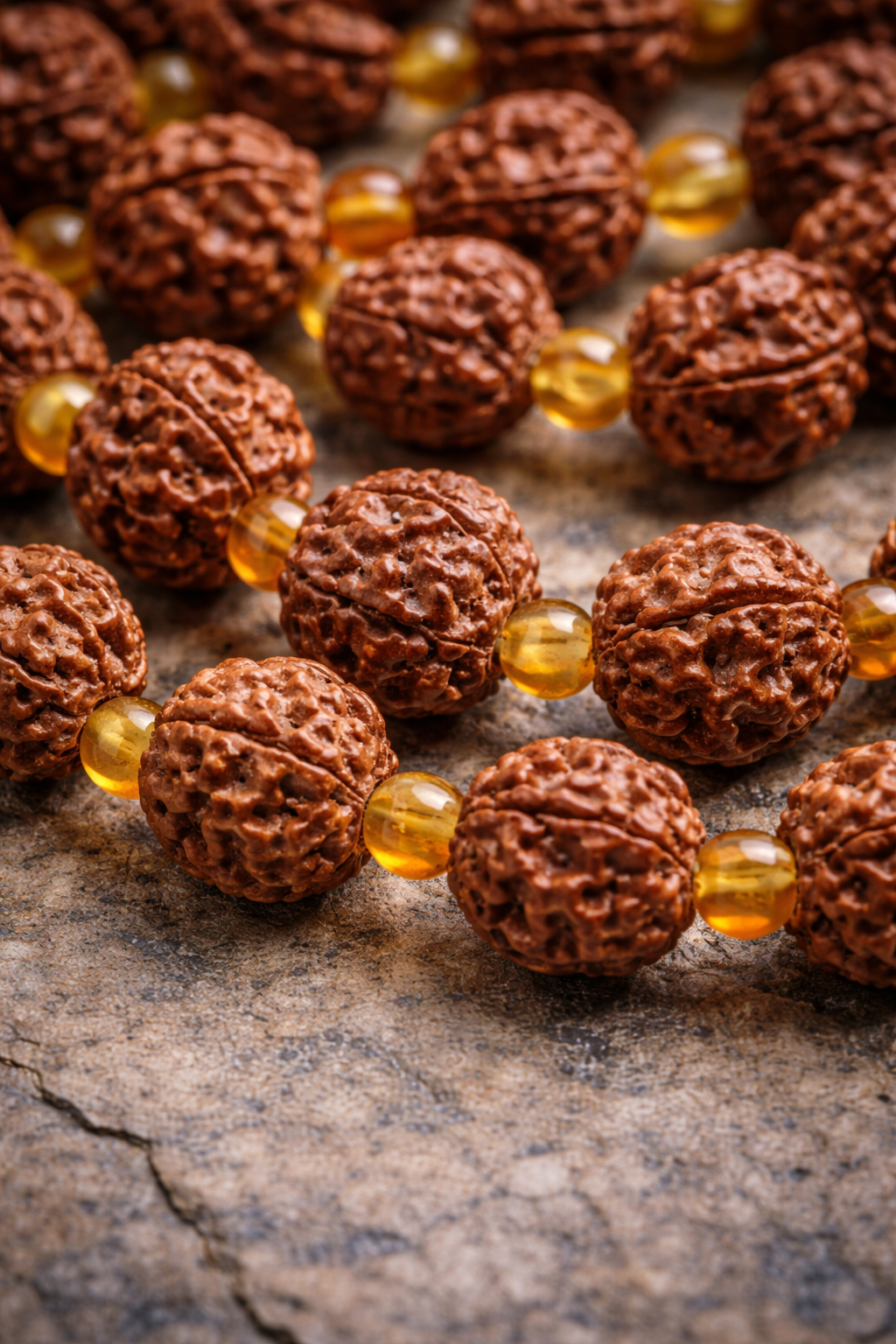 Close-up of handcrafted Rudraksha mala beads with golden amber spacers on a textured stone surface, highlighting the natural bead texture and warm amber tones.