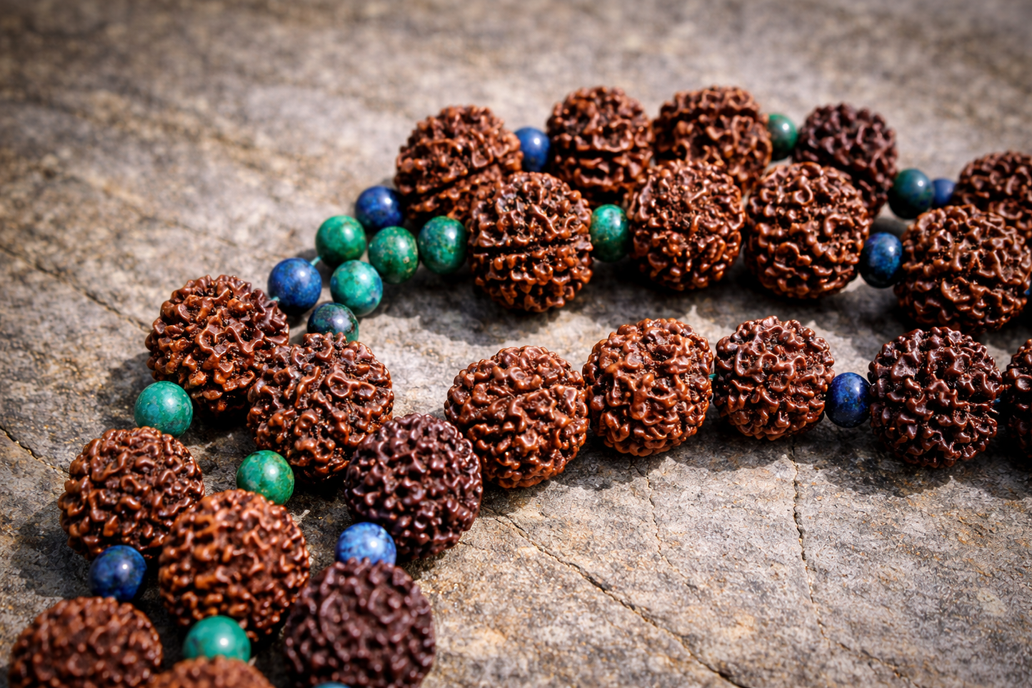 Close-up of handcrafted Rudraksha mala beads laid on natural stone, accented with Azurite Malachite and African Turquoise gemstone beads, highlighting the rich textures and earthy colors of the spiritual necklace.