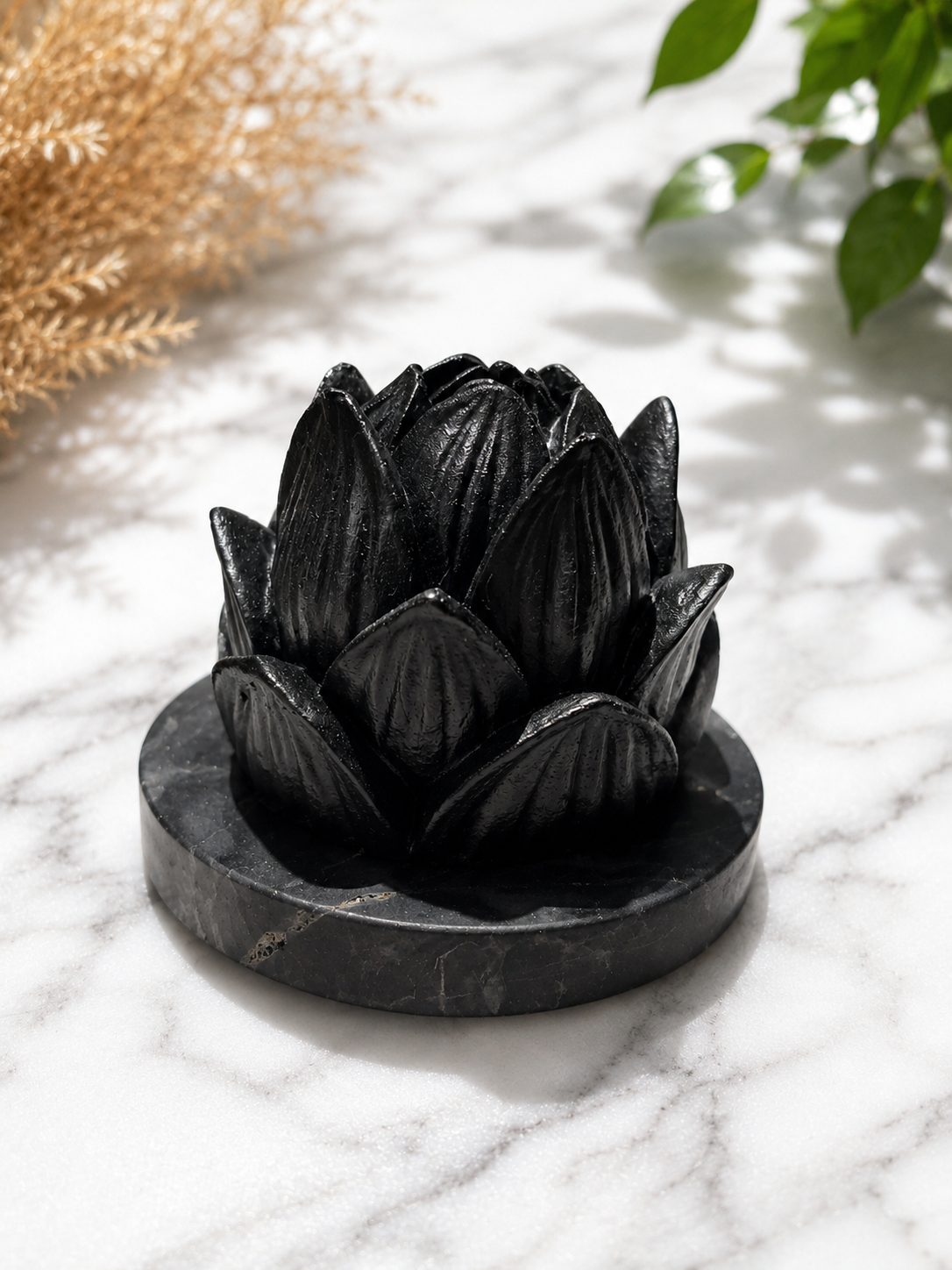 Handcrafted black shungite lotus candle holder on a polished stone base, photographed on a white marble surface with soft natural lighting and botanical styling.
