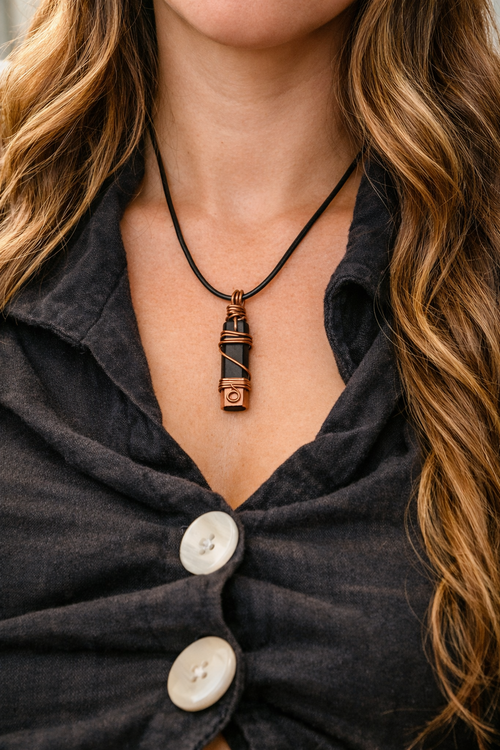 Close-up of a woman wearing a copper-wrapped shungite pendant on a black cord, styled with long wavy hair and soft natural lighting.