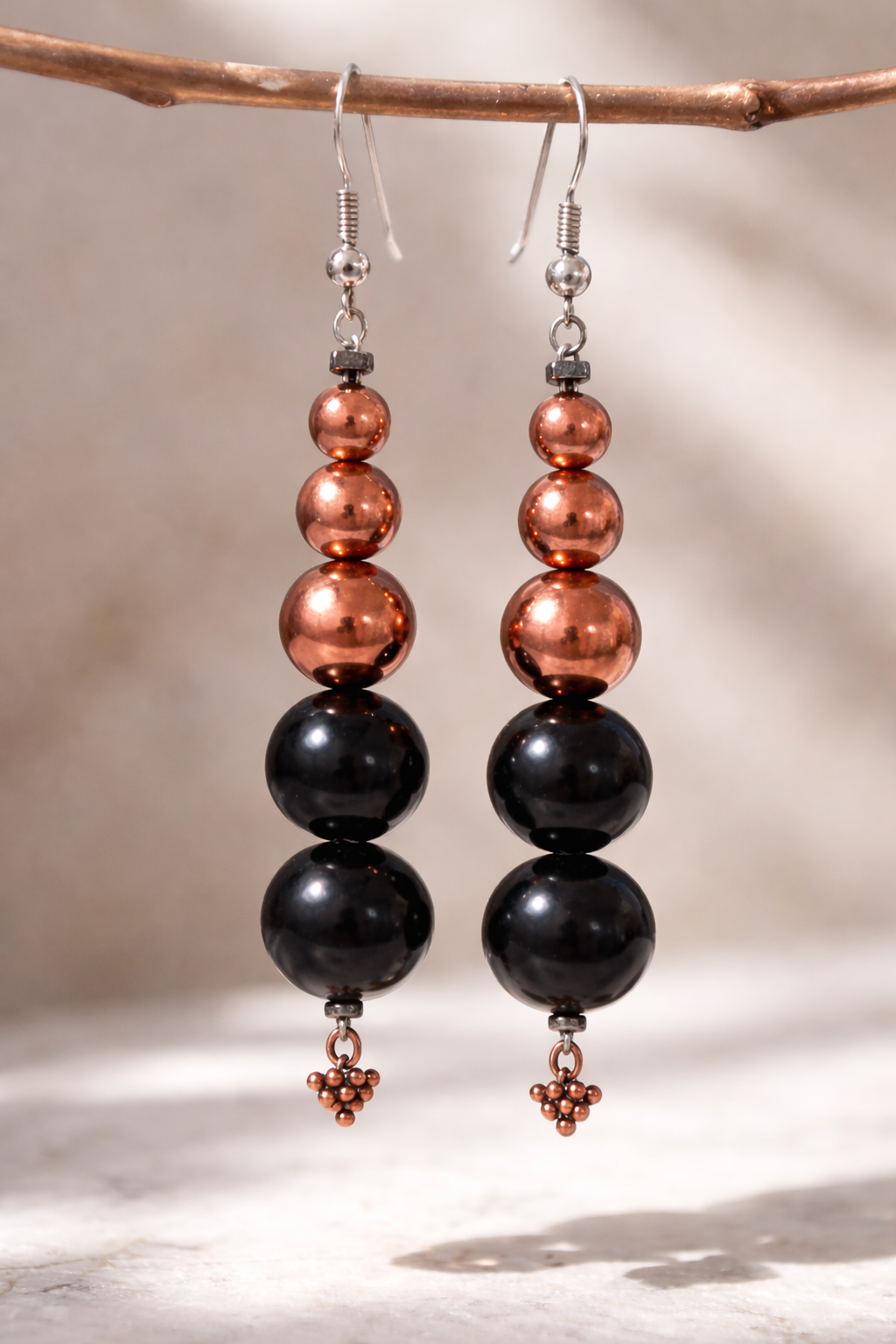 Handmade shungite and copper bead drop earrings hanging from a branch with soft natural lighting and neutral background