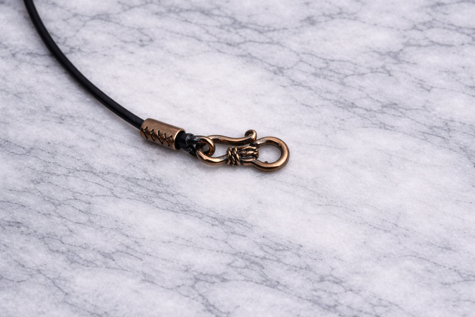 Copper necklace clasp with two black leather cords on white marble background