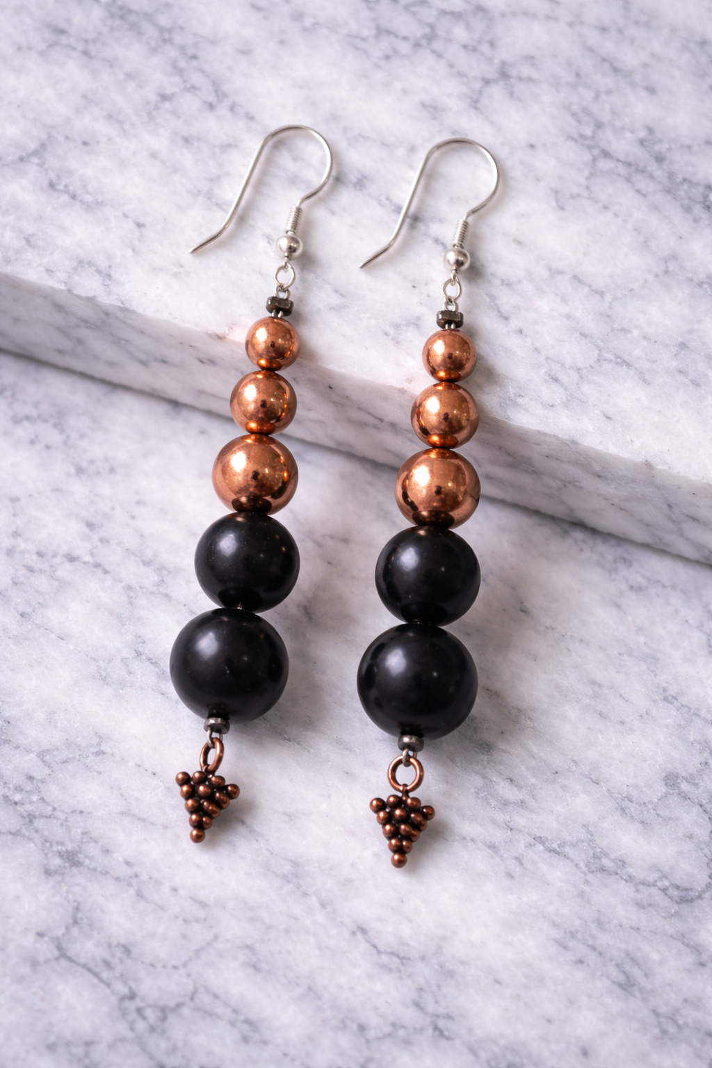 Handmade shungite and copper bead drop earrings displayed on a light marble surface with soft natural lighting