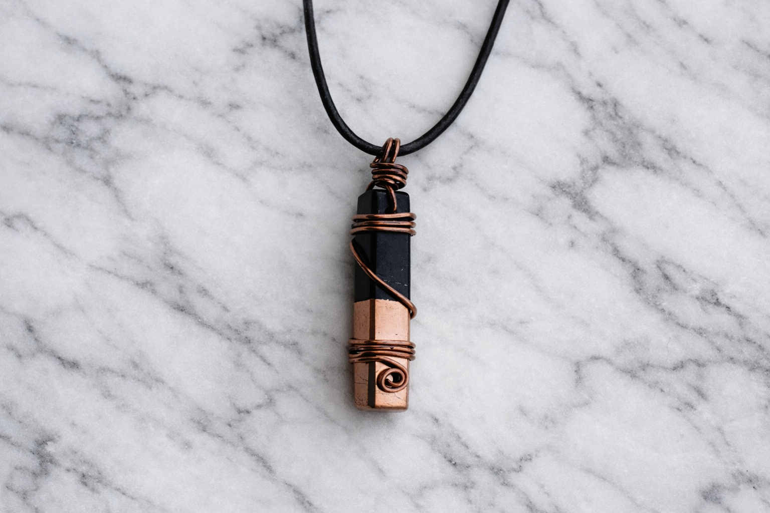 Handmade shungite and copper wire-wrapped pendant on white marble background