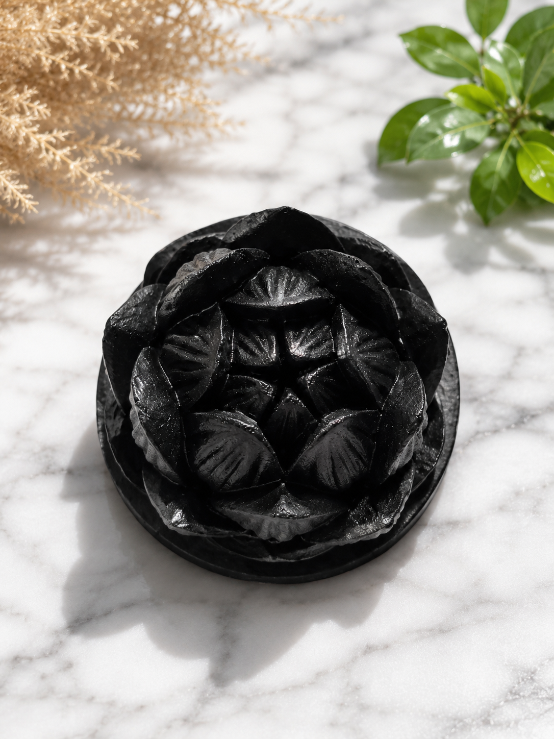 Hand-carved black shungite lotus candle holder displayed on a white marble surface with soft natural lighting, detailed petal texture, and calming botanical background accents.