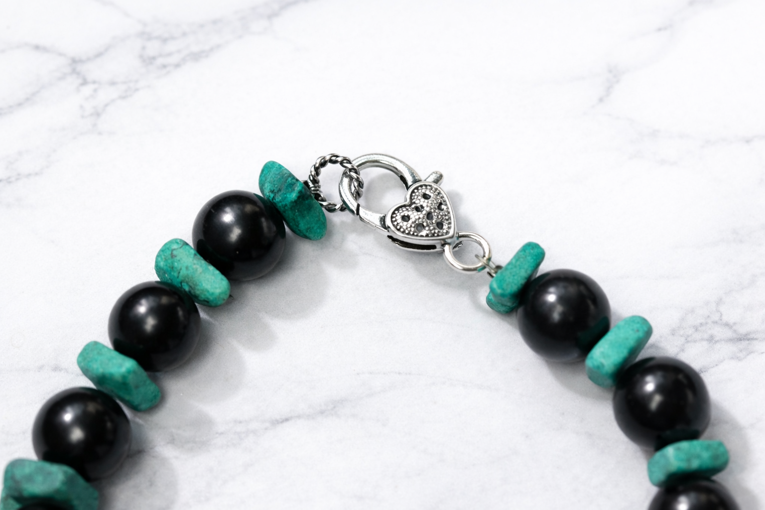 Close-up of handmade shungite and turquoise necklace with silver heart clasp on marble background