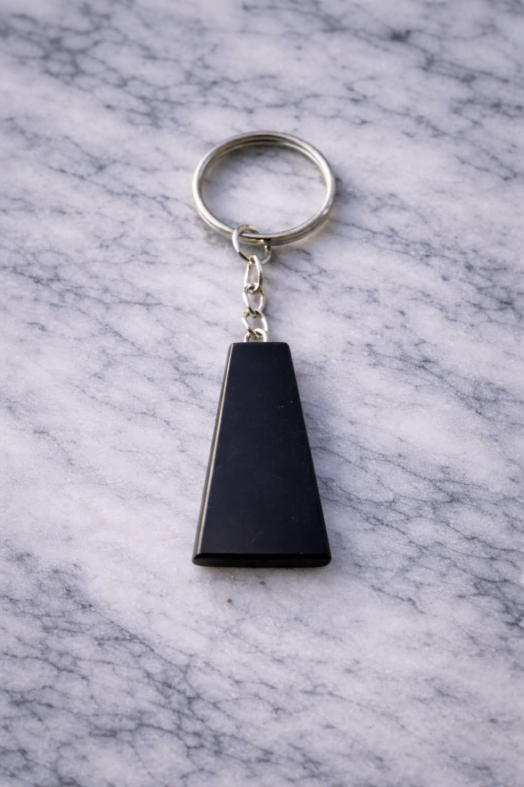Polished black shungite trapezoid keychain with silver ring, displayed on white marble surface.