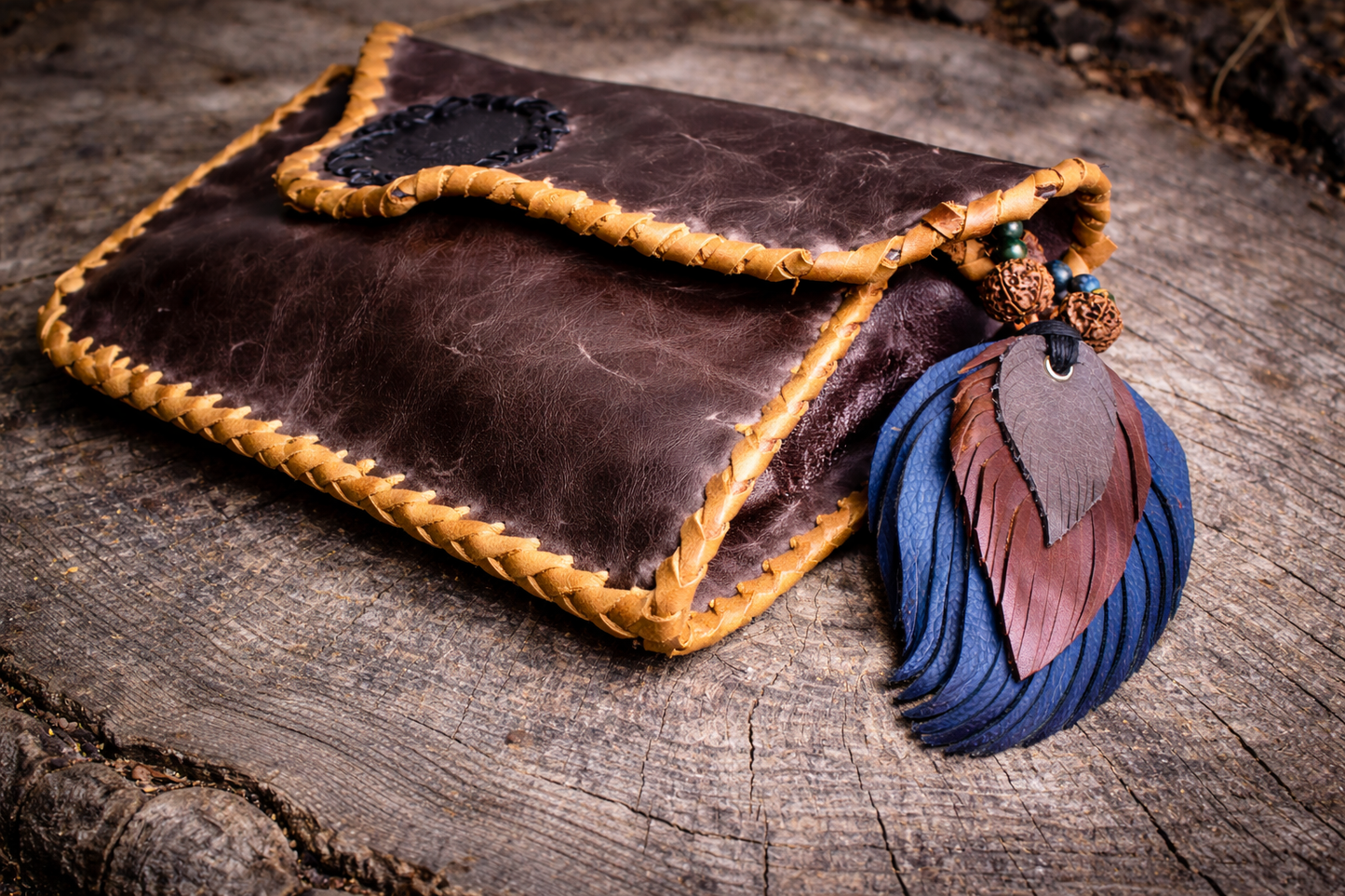“Handcrafted dark brown leather pouch with braided stitching and black Sanshara stamp, resting on a natural stone surface, finished with a blue and brown leather tassel.”