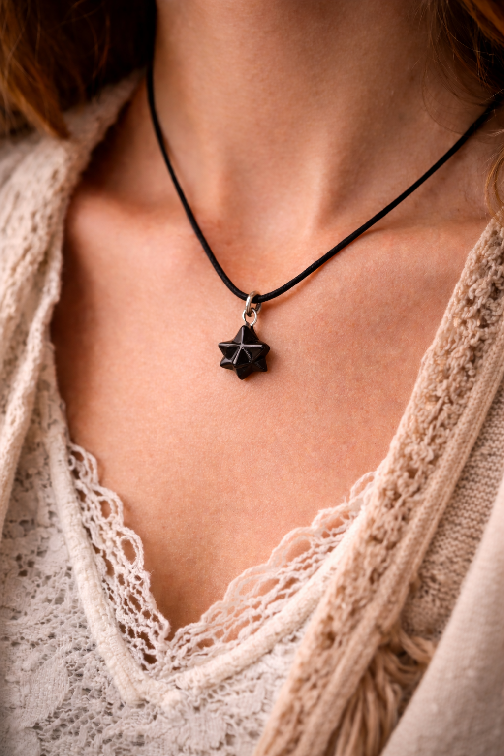 Small black shungite merkaba pendant on a black cord, worn on a woman’s chest with soft natural light and neutral boho clothing.