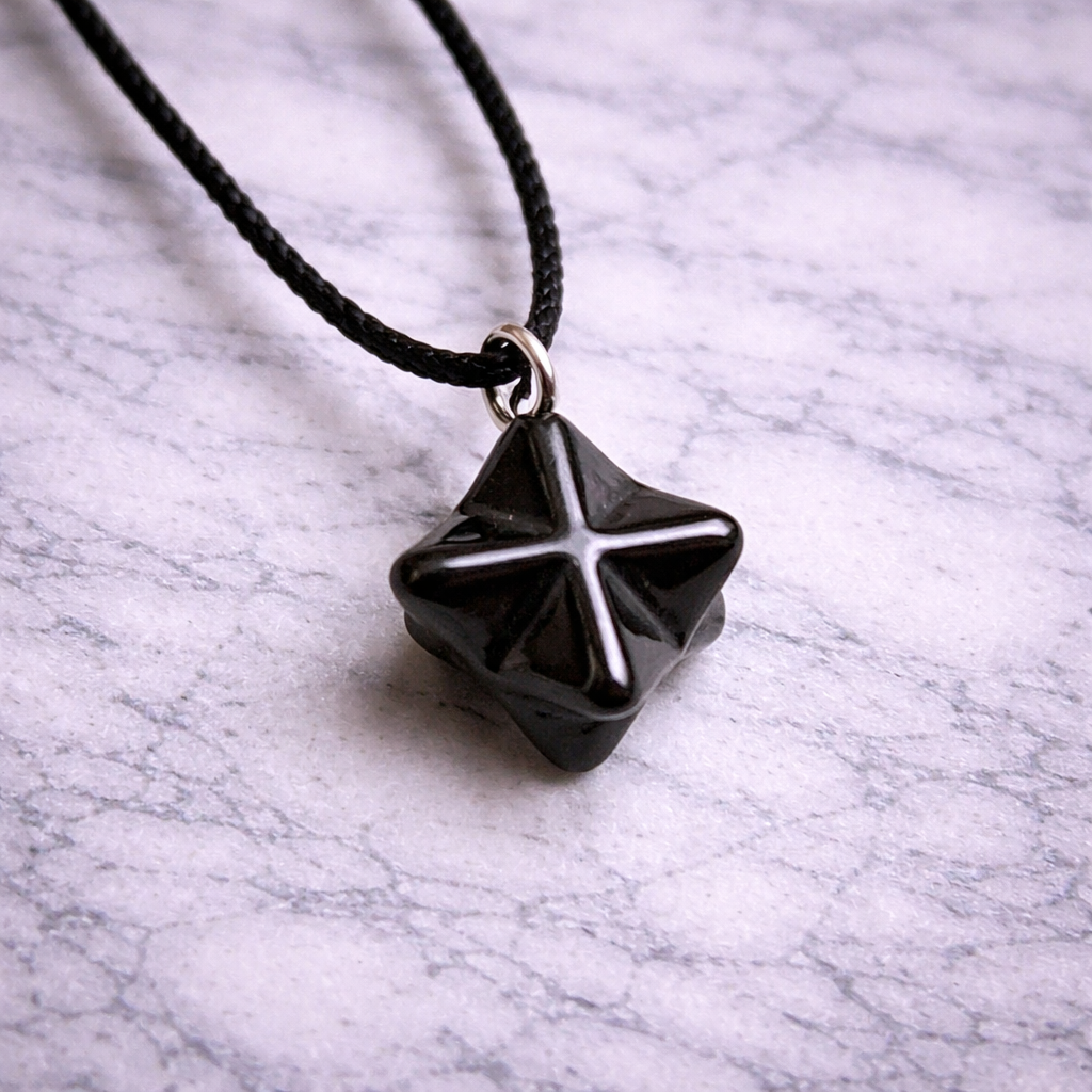 Shungite merkaba pendant on black cord resting on white marble surface”