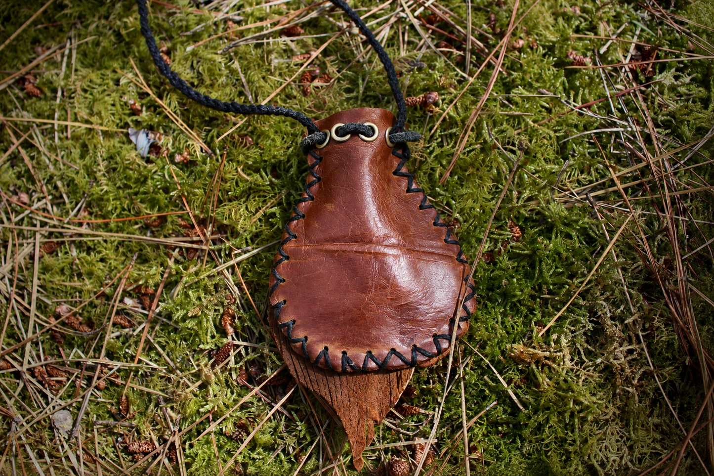 Handcrafted brown leather crystal pouch necklace resting on moss in a forest, designed to hold a small crystal or stone.