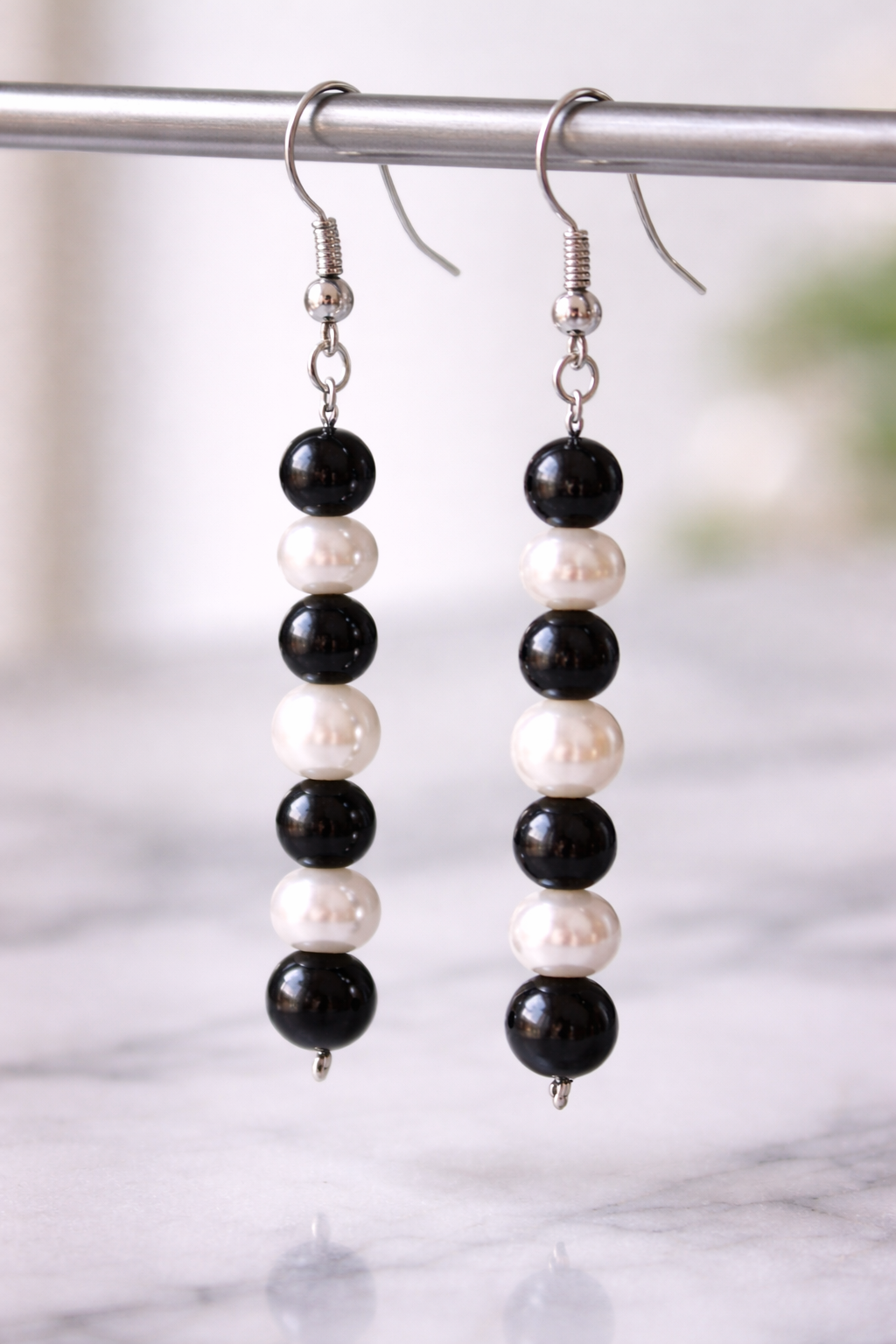 Close-up of handmade drop earrings featuring alternating black shungite beads and white freshwater pearls, displayed on a light marble surface with soft natural lighting.