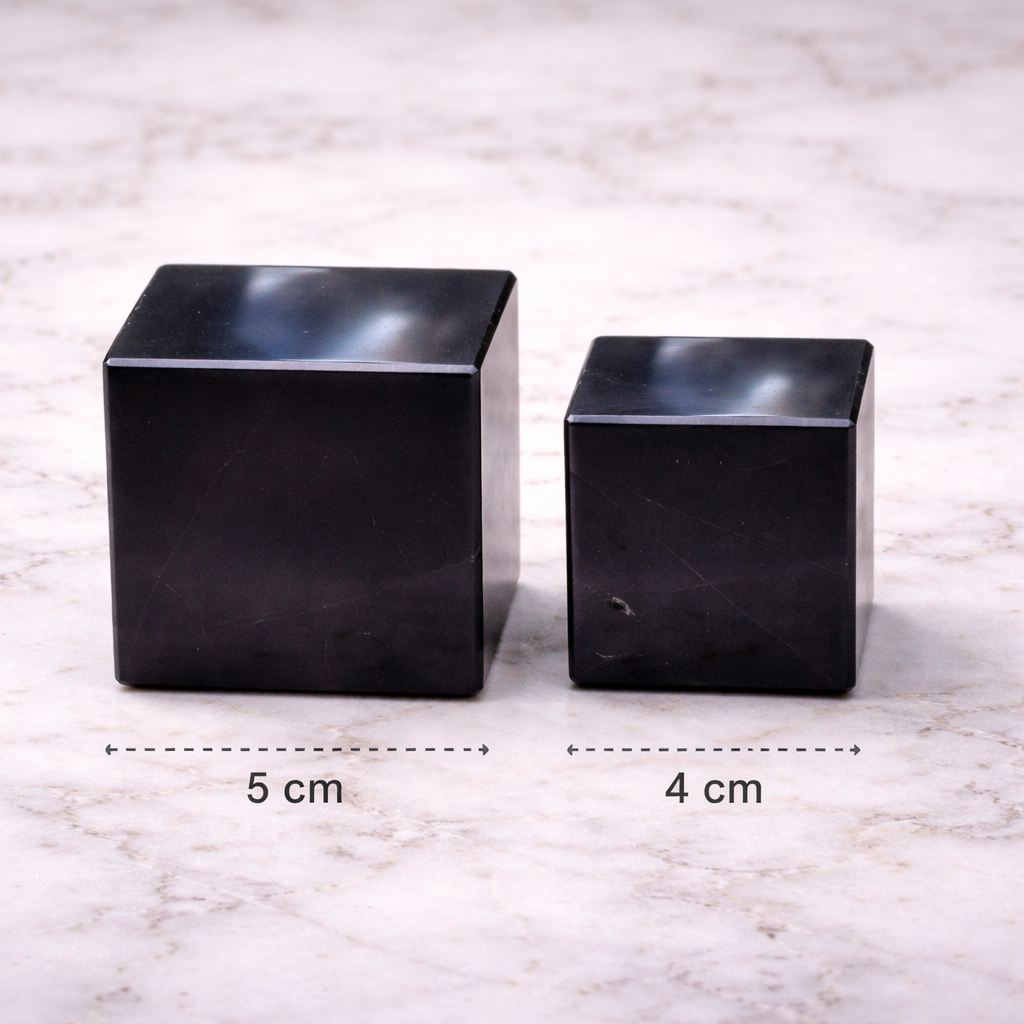Two polished shungite cubes on white marble surface showing size comparison, 5 cm and 4 cm crystal harmonizer blocks.