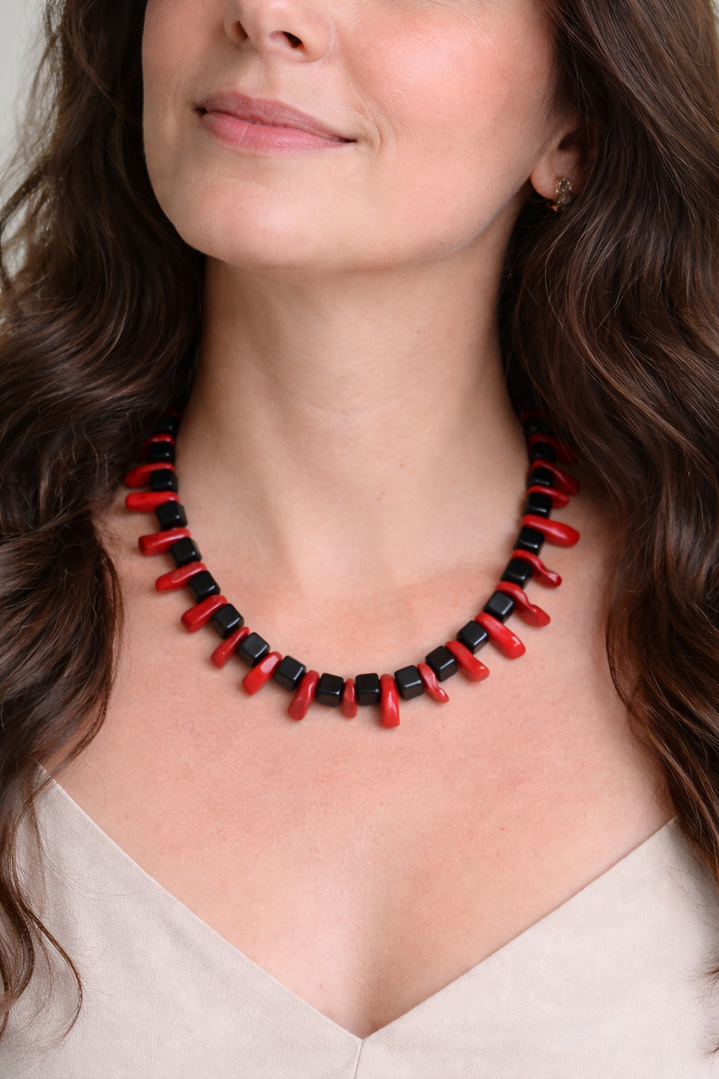 Shungite cube and red coral bead necklace worn on model against a soft neutral backdrop with natural lighting