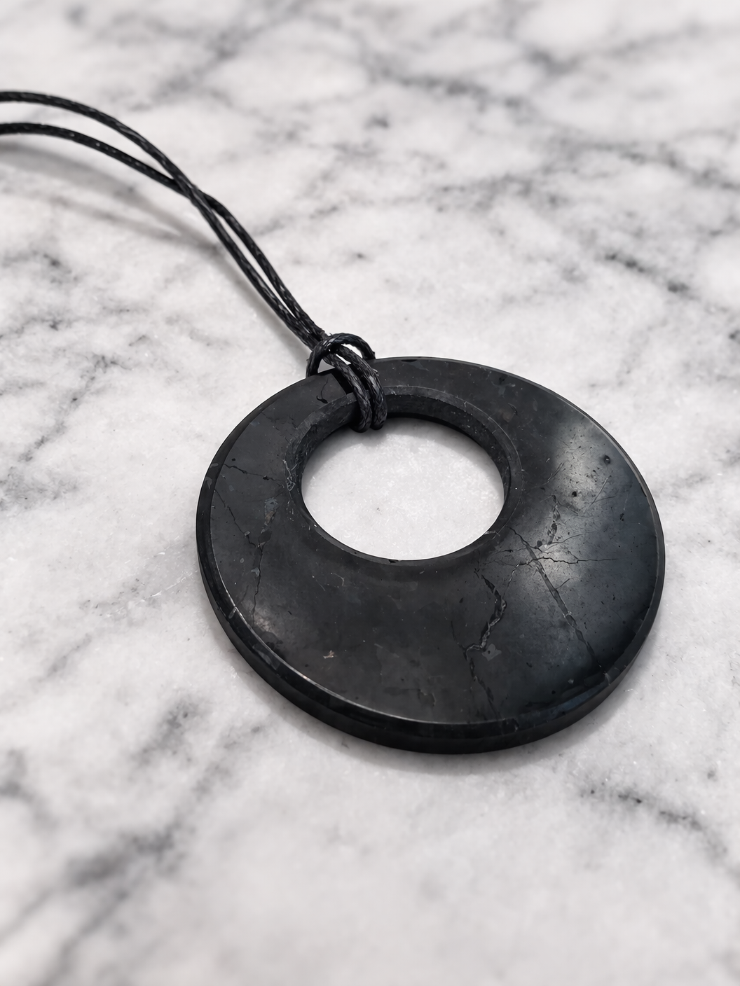 Real shungite donut pendant necklace on black cord displayed on white marble background