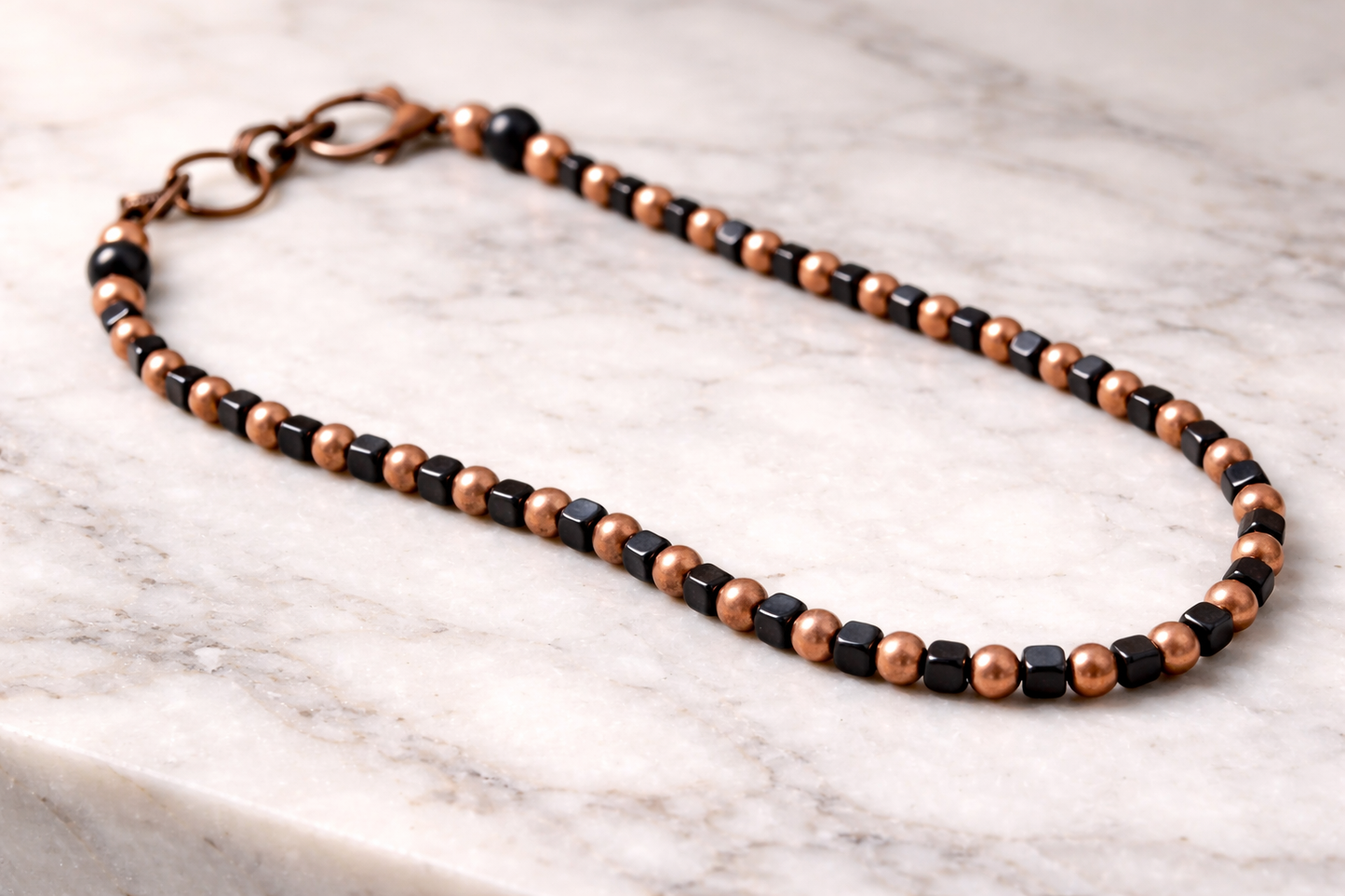 Handmade shungite cube and copper bead necklace arranged on a light marble surface with soft natural lighting