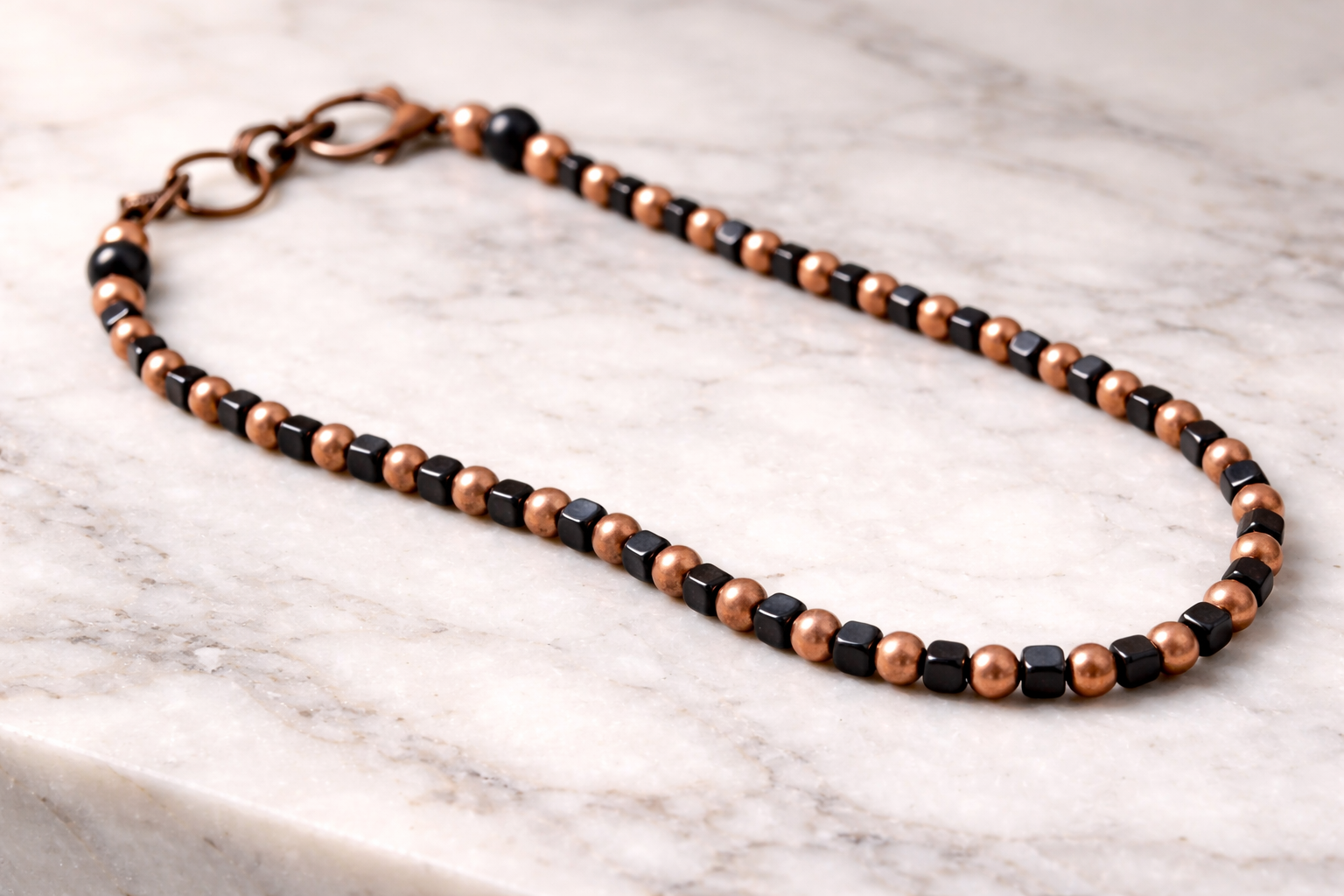 Handmade shungite cube and copper bead necklace arranged on a light marble surface with soft natural lighting
