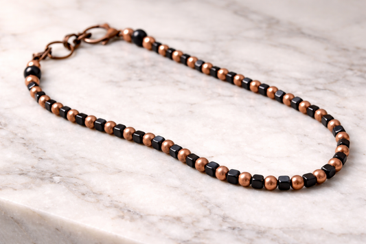 Handmade shungite cube and copper bead necklace arranged on a light marble surface with soft natural lighting
