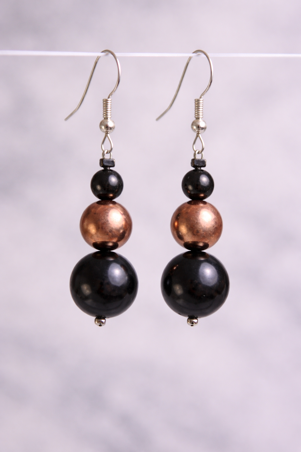 Handmade shungite and copper bead drop earrings hanging from silver hooks against a soft neutral background