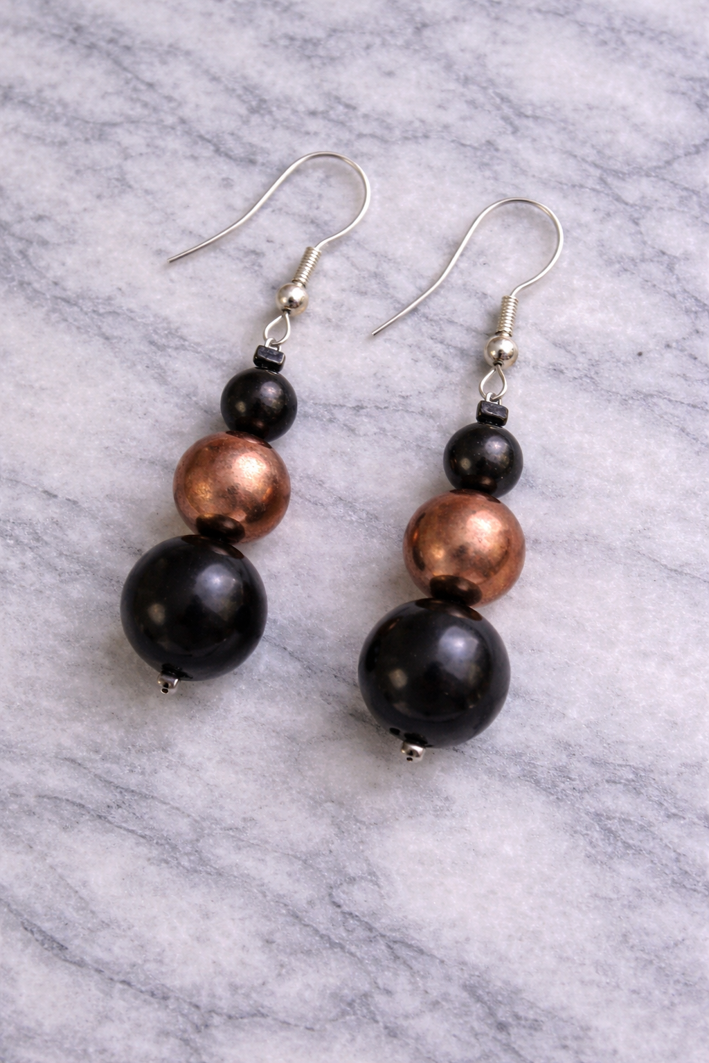 Shungite and copper bead dangle earrings on a light gray marble surface with silver hooks