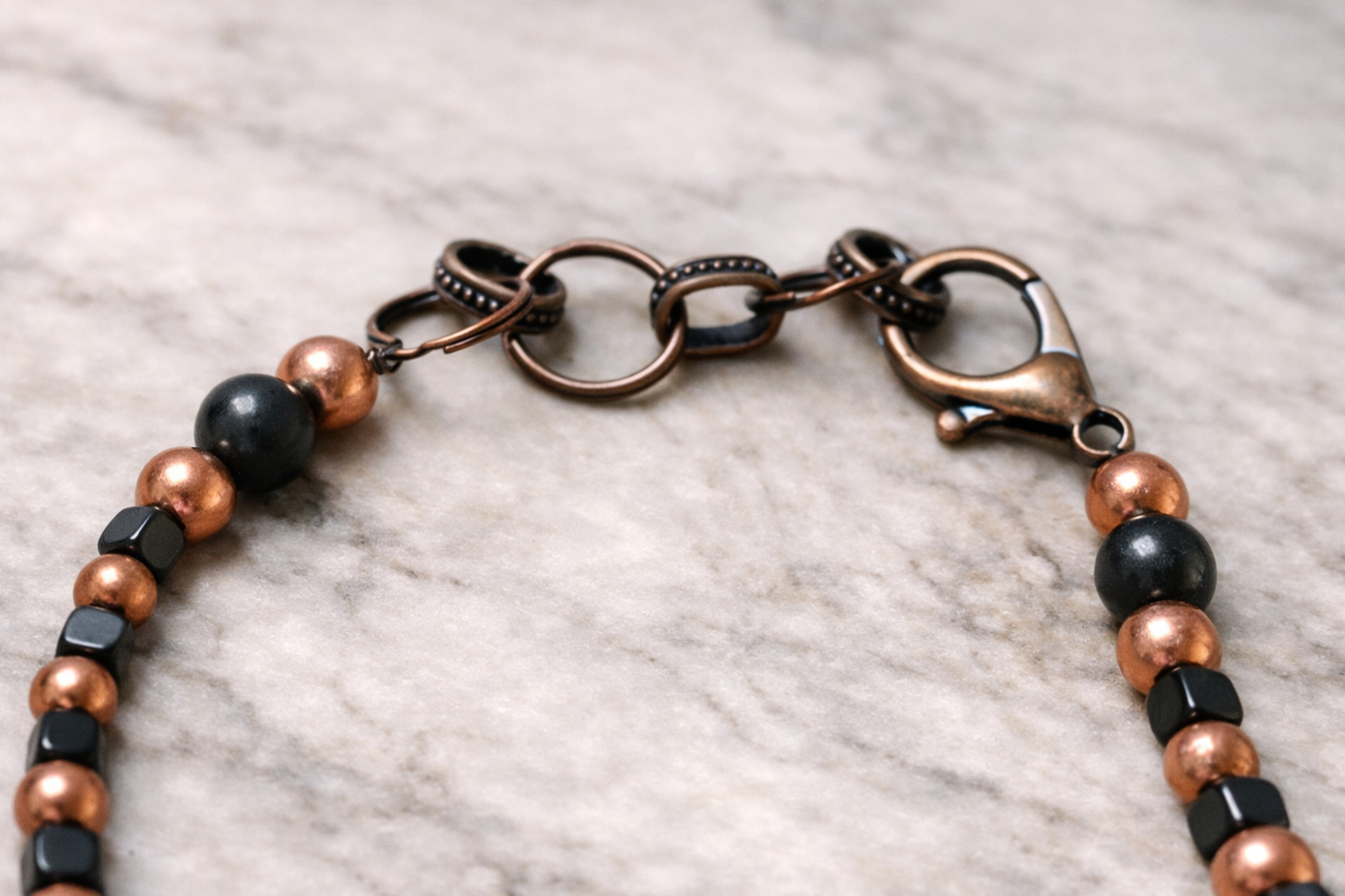 Close-up of handmade shungite and copper bead necklace clasp on a light marble surface with soft natural lighting