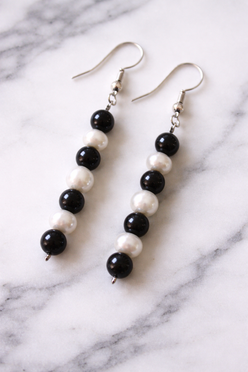 Close-up of handmade drop earrings featuring alternating black shungite beads and white freshwater pearls, displayed on a light marble surface with soft natural lighting.