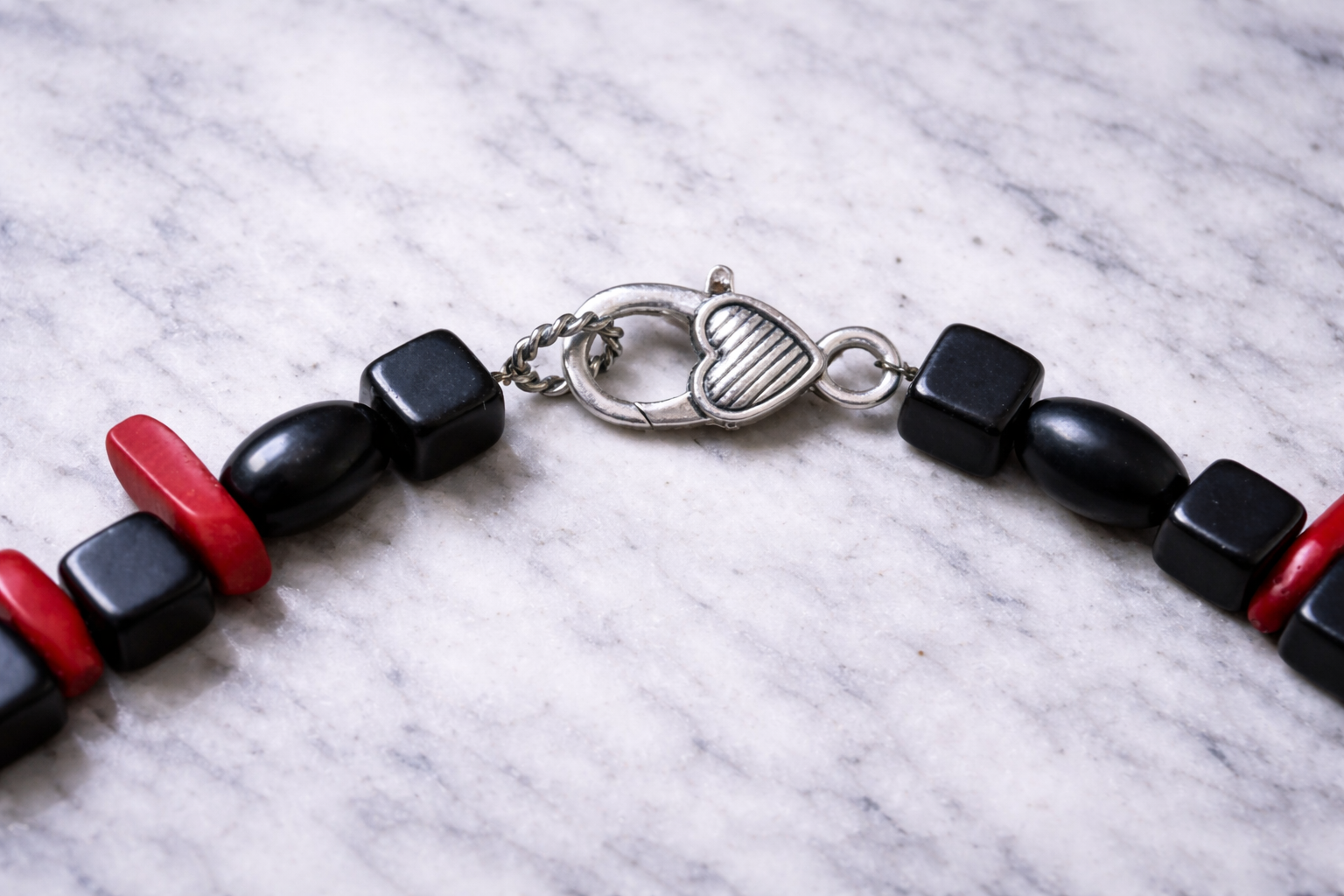 Close-up of silver lobster clasp with black shungite cube beads and red coral accents on a light marble surface with soft natural lighting
