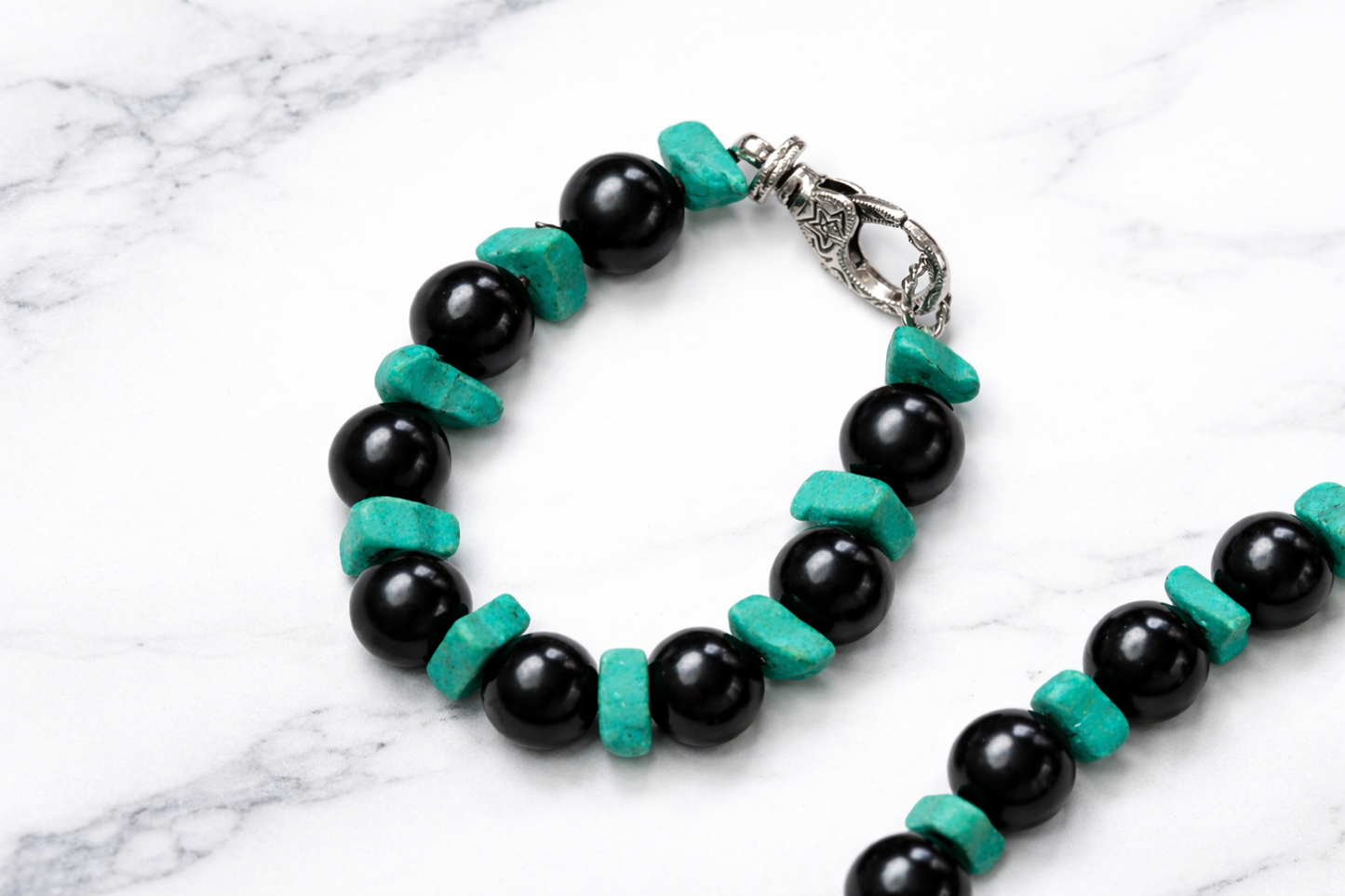 Handmade shungite and turquoise beaded bracelet with silver clasp on white marble background