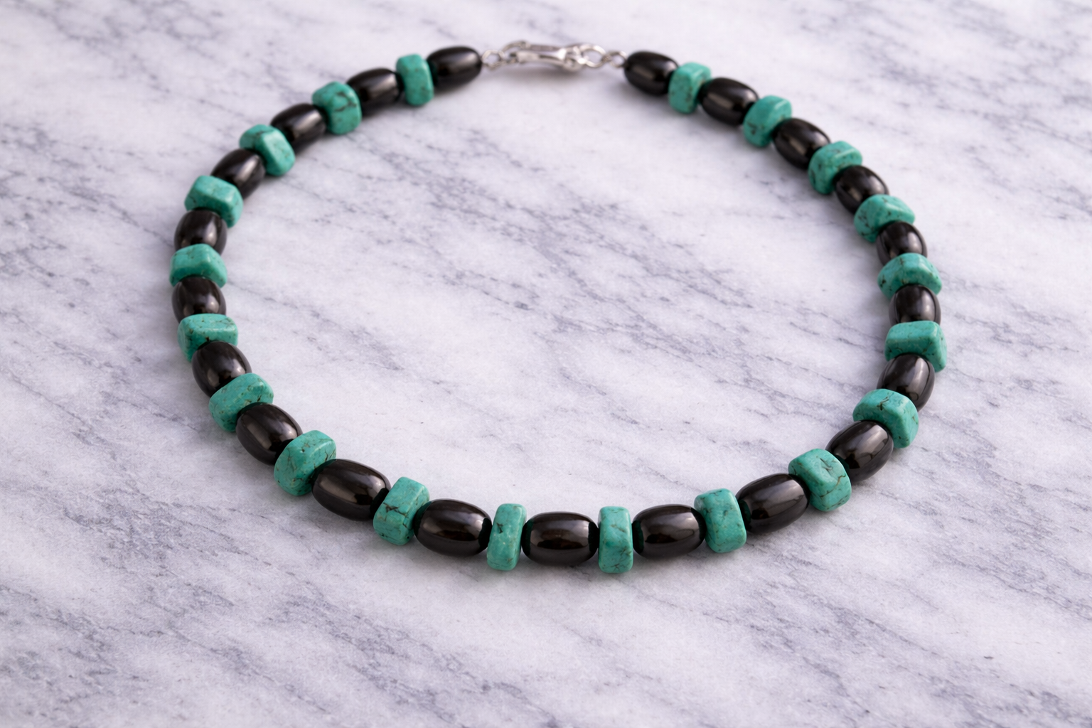 Shungite and turquoise beaded necklace arranged in a circle on a white marble surface, featuring alternating glossy black shungite beads and natural turquoise stones with a silver clasp.
