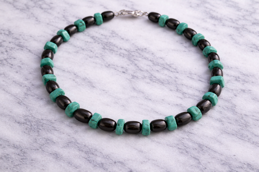 Shungite and turquoise beaded necklace arranged in a circle on a white marble surface, featuring alternating glossy black shungite beads and natural turquoise stones with a silver clasp.