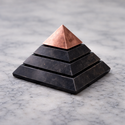 Stepped shungite pyramid with copper tip on light marble surface in soft natural light