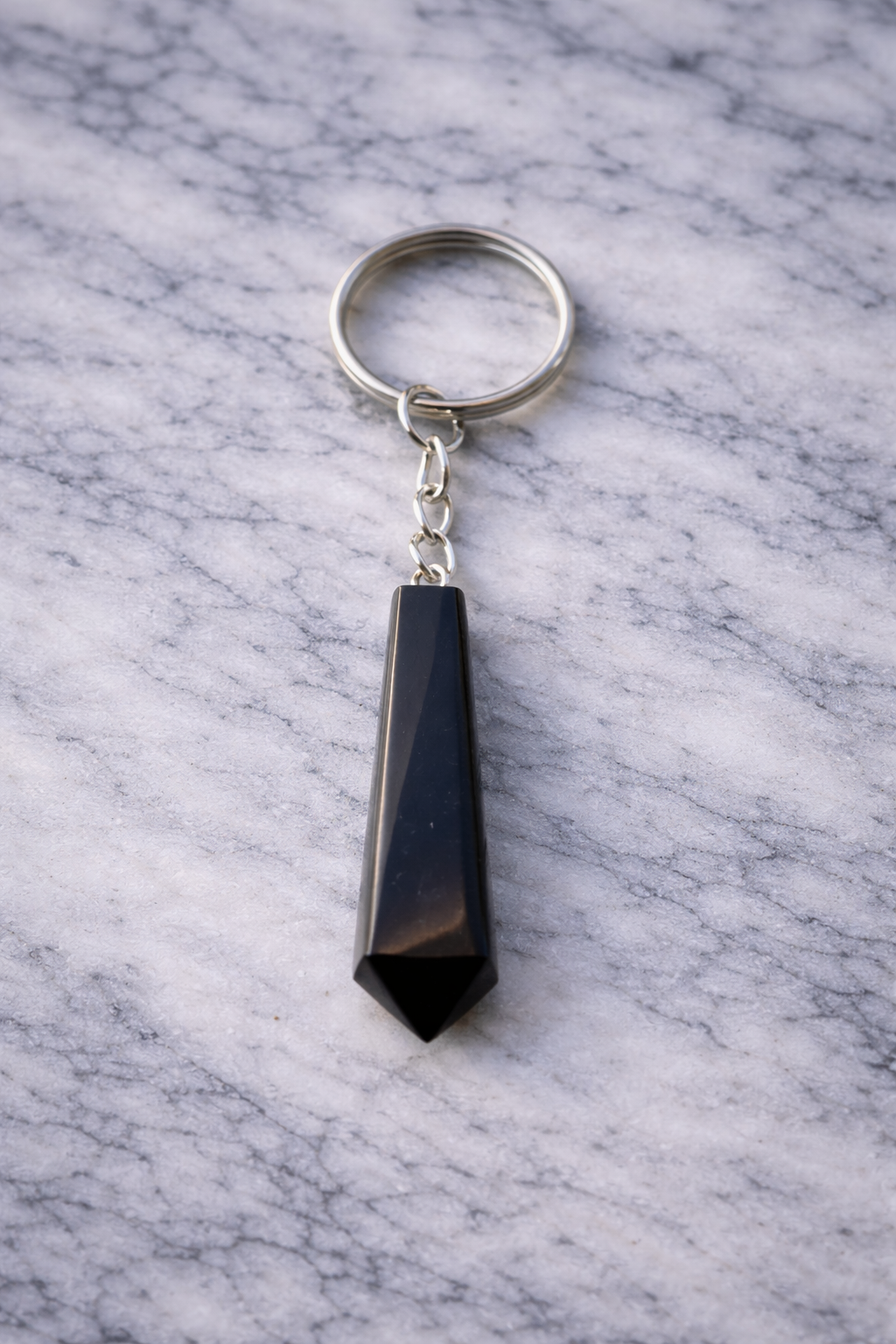 Pointed black shungite keychain with silver ring resting on white marble surface in soft natural light.