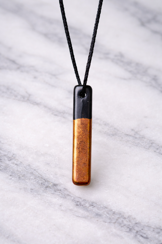“Two-tone shungite and copper pendant hanging on black cord against smooth marble background”
