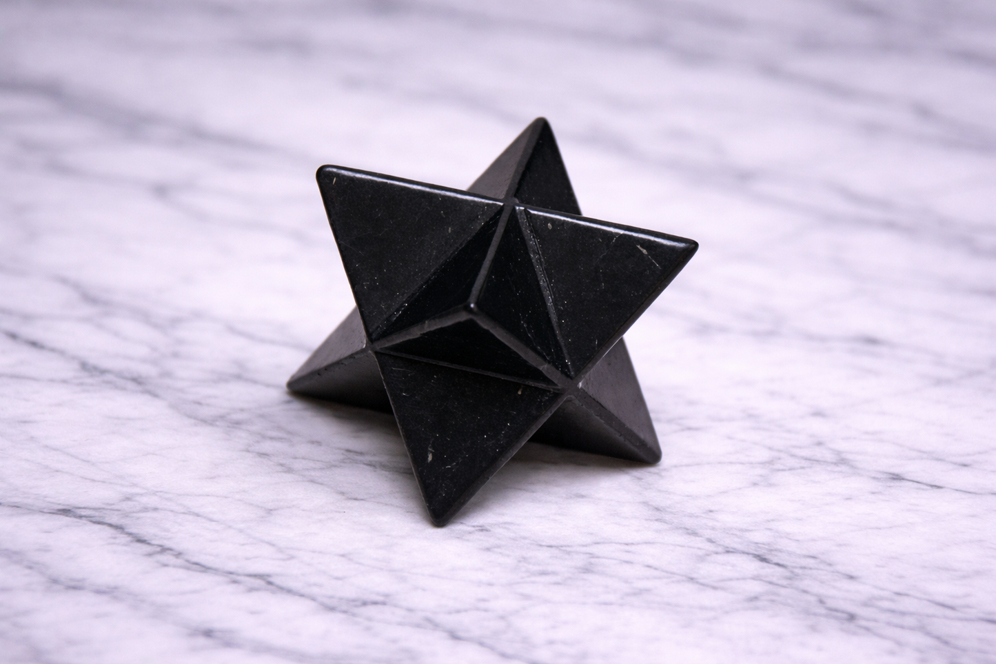 “Black shungite merkaba star photographed from side angle on white marble”