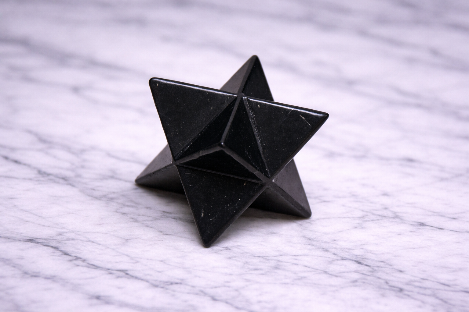 “Black shungite merkaba star photographed from side angle on white marble”