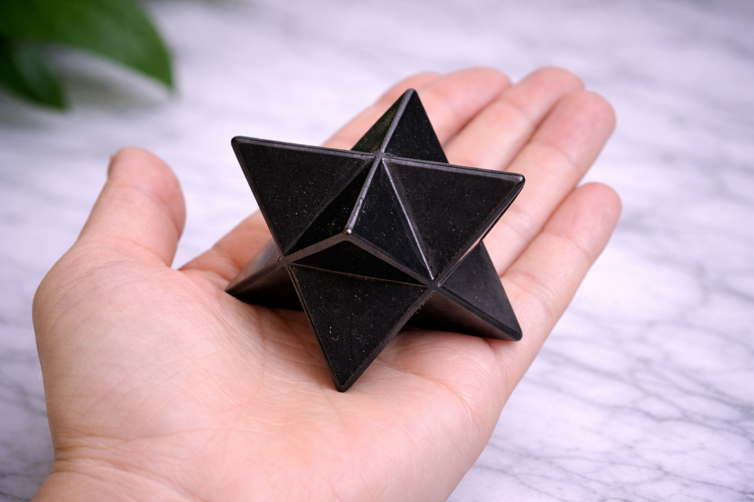 “Hand holding black shungite merkaba star over smooth marble background”