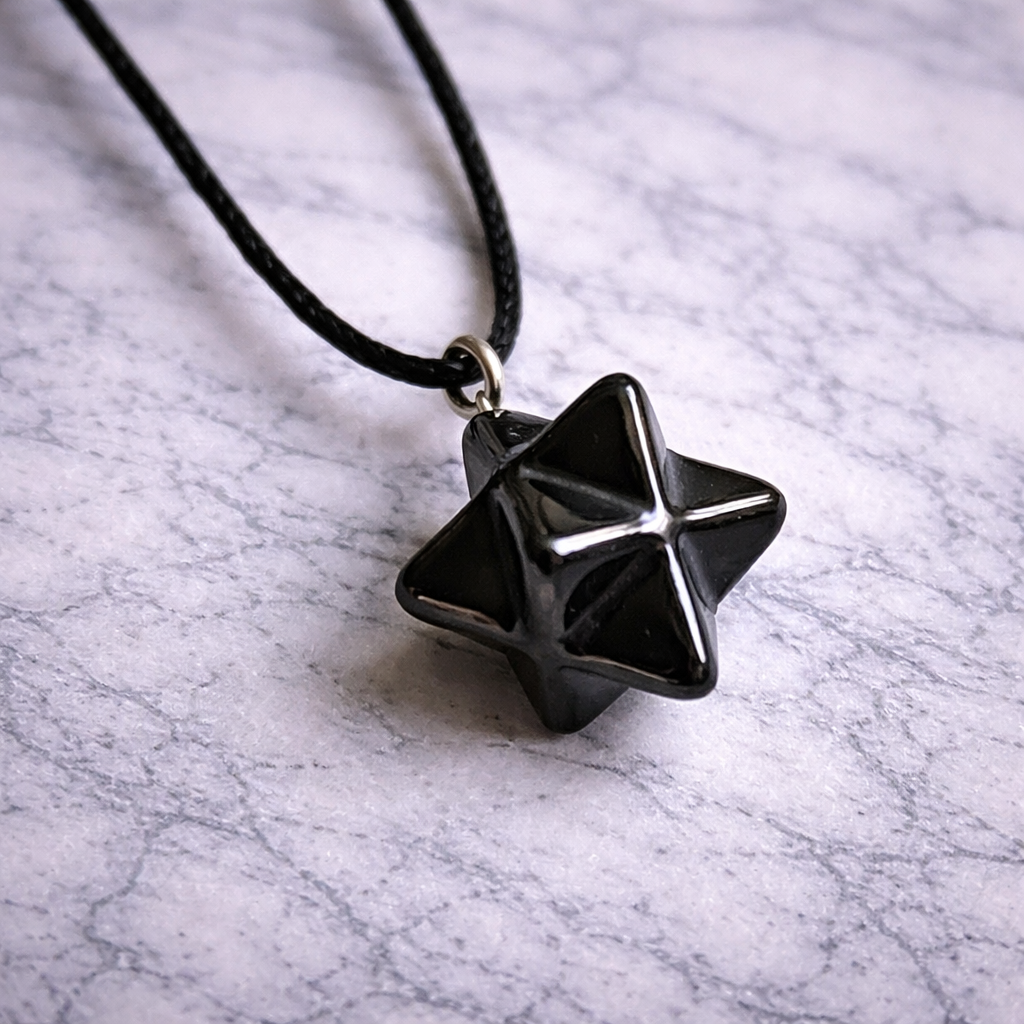 Shungite merkaba pendant on black cord resting on white marble surface”