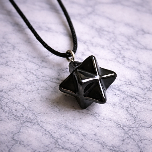 Shungite merkaba pendant on black cord resting on white marble surface”