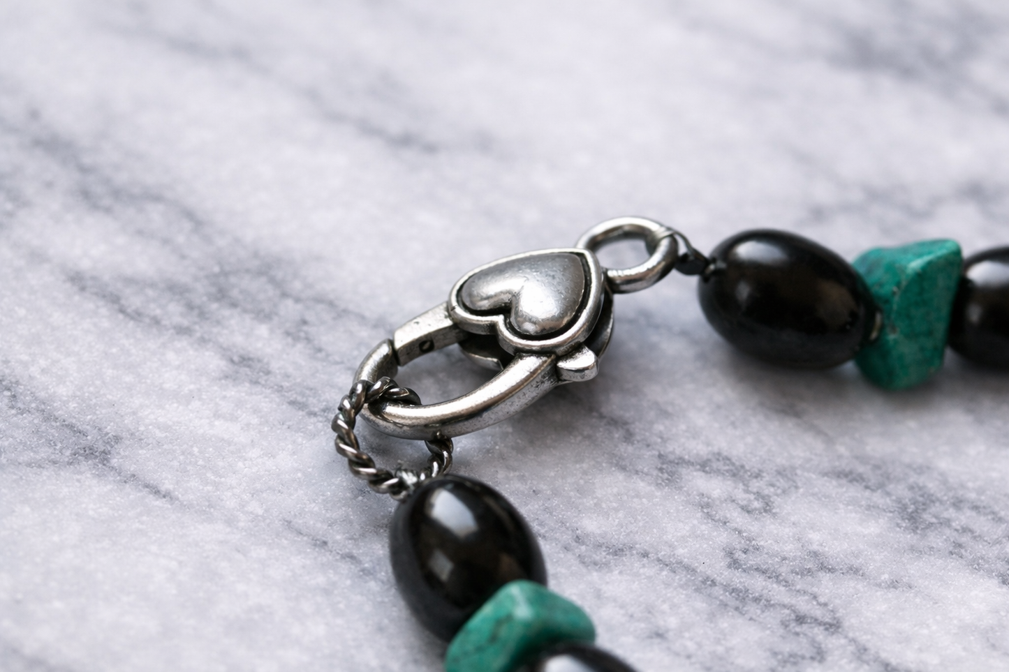 Shungite and turquoise beaded necklace arranged in a circle on a white marble surface, featuring alternating glossy black shungite beads and natural turquoise stones with a silver clasp.