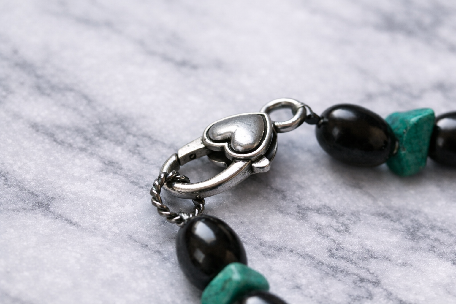 Shungite and turquoise beaded necklace arranged in a circle on a white marble surface, featuring alternating glossy black shungite beads and natural turquoise stones with a silver clasp.
